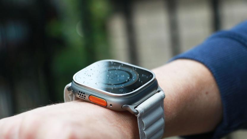 Off-angle view of the Apple Watch Ultra with alpine loop on a person's wrist. From this perspective, the orange Action button and speaker grill on the left edge are in view, while the screen's contents are dim.