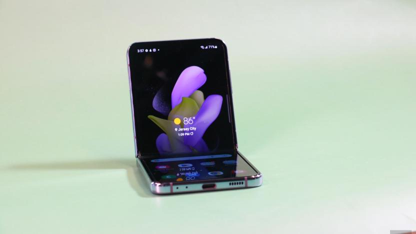 The Galaxy Z Flip 4 half folded and sitting up on a green surface with its screen facing out.