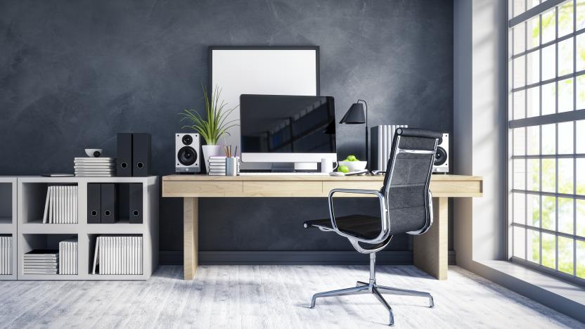 Interior of a modern home office next to a big window. Light wood desk with organized set up of books, office supplies and computer with some room decor around it.