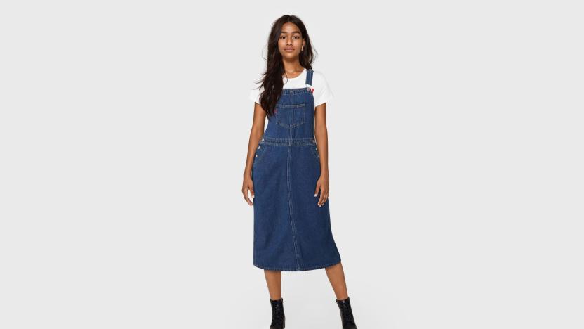 An AI-generated (fake) young woman wearing a Levi's overall dress in front of a gray background.