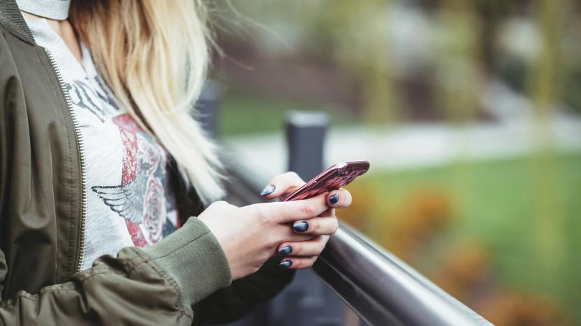 The torso of what appears to be a young woman holds a smartphone while standing next to a railing.