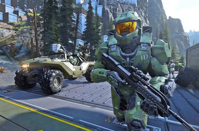 The mech-suit clad Master Chief runs down a road alongside a Warthog jeep-like vehicle in this promo still from the video game 'Halo Infinite'.
