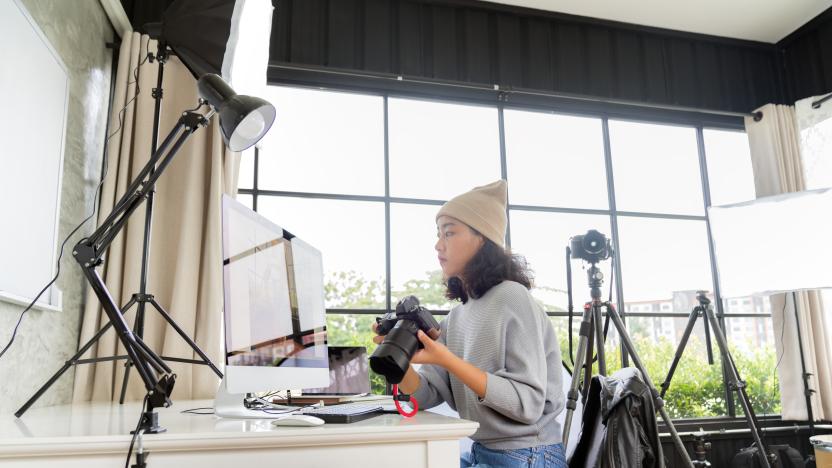 Side view of female freelancer photographer checking photos on a digital camera while sitting at the table in workstation.freelancer photographer