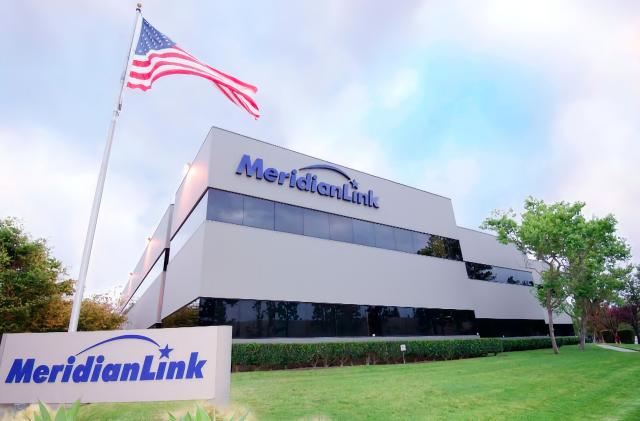 Company photo of MeridianLink headquarters. A modern building with company logo behind a green lawn with a sign (also bearing the company logo) and an American flag.