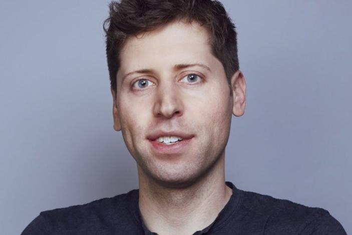 Headshot of OpenAI CEO Sam Altman. He looks into the camera with a partial smile against a grayish background.