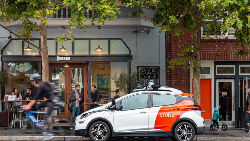 A white sedan with orange Cruise branding parked on the side of the street. In the background is a coffee shop.