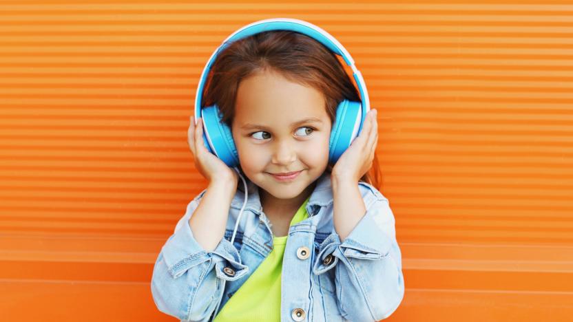 Portrait of happy smiling child in headphones listening to music on city street over orange wall background
