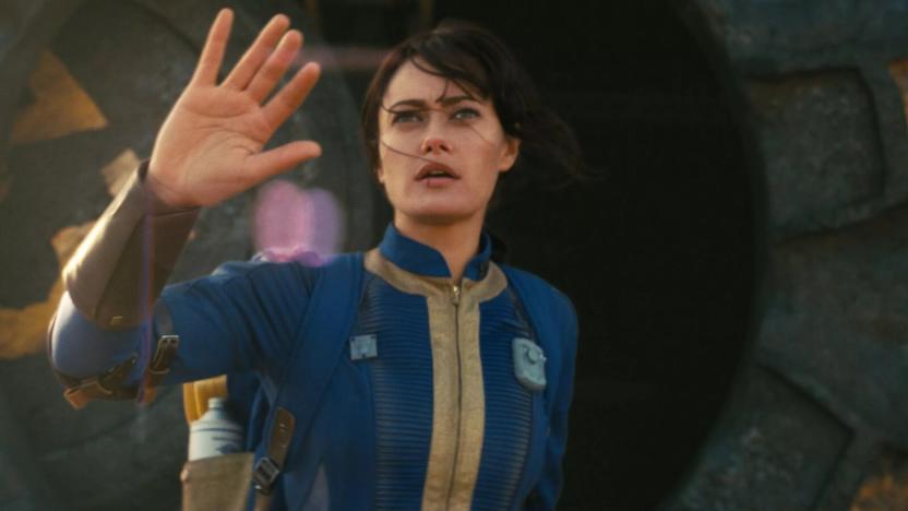 Still from the upcoming "Fallout" TV series. Ella Purnell ("Yellowjackets") stands waving with a hesitant look on her face. She wears a blue uniform with gold trim.