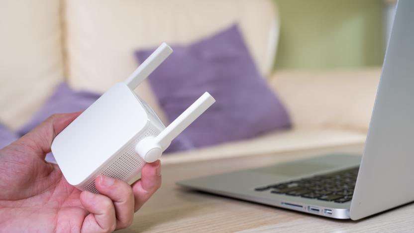 Selective focus at range extender. Internet router on working table with blurred man connect the cable at the background. Fast and high speed internet connection to cover home network usage.