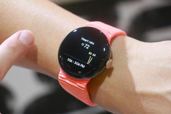 The Pixel Watch 2 with a peach woven band on a wrist, showing a heart rate reading.