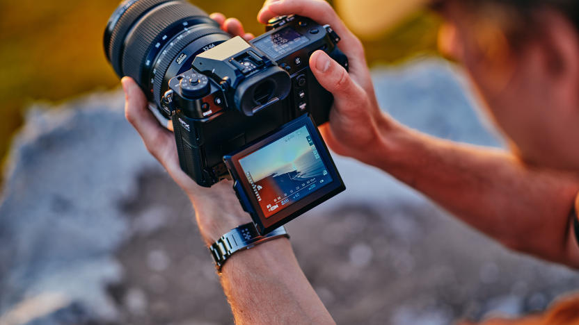 A person holding the Fujifilm GFX 100S II camera with its viewfinder folded out. View from slightly above their left shoulder.