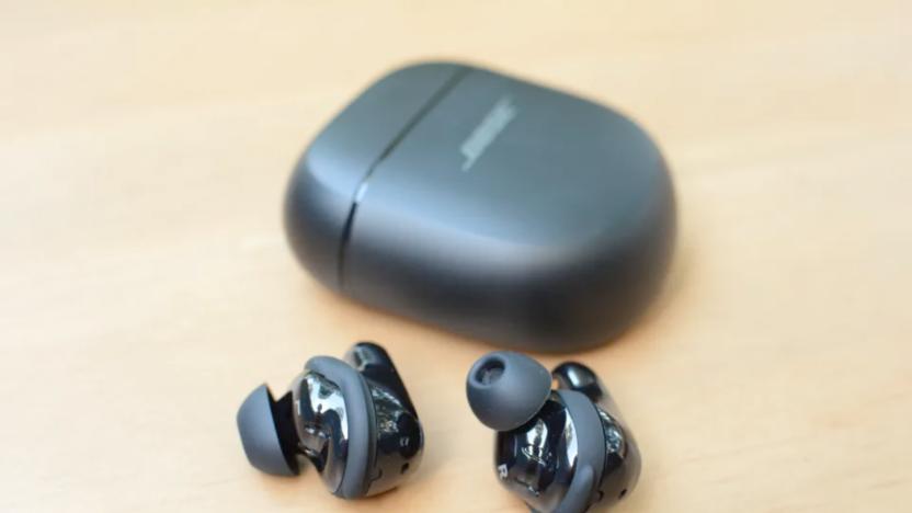 A pair of earbuds on a table next to a charging case. 