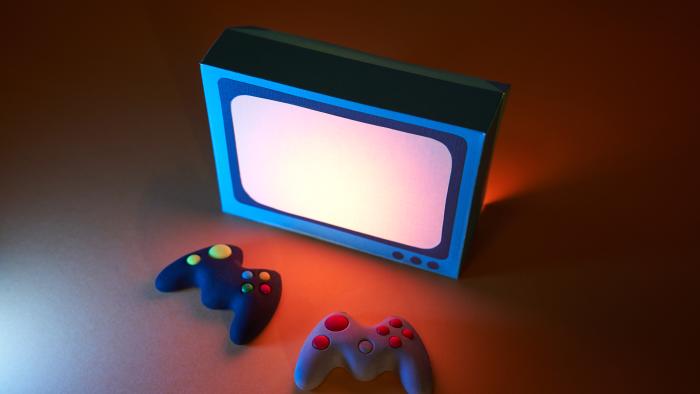 High angle view of two game controllers in front of a retro-style television. The screen light illuminates the game controllers. Video games concept.