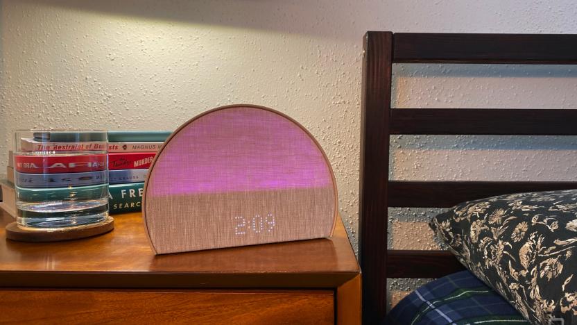 The Hatch Restore 2 sleep machine sits on my bedside table. There's a glass of water and a stack of books in the background. The bed's headboard and pillow are to the right of the image. 