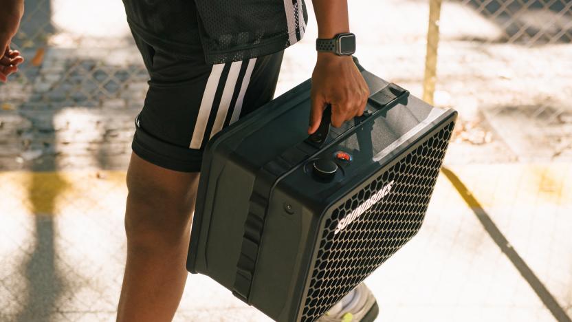 Someone in workout clothes carries a Soundboks Go Bluetooth speaker into a basketball court.