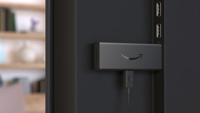 Product photo of the Amazon Fire TV Stick 4K Max streaming stick. View of the back of a TV: closeup of the streaming stick inside its HDMI port. Blurred living room background in view. 