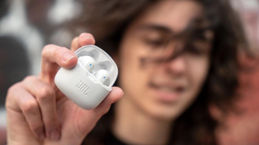 A young man holding white JBL Tune Flex earbuds.