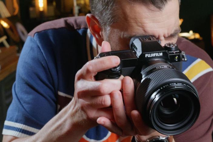 A man holding the Fujifilm GFX100S II up to his eye, with the lens pointing out.