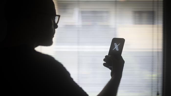 The X logo is seen on a mobile device held in the hand of a man with glasses in this illustration photo in Warsaw, Poland on 29 August, 2023. (Photo by Jaap Arriens/NurPhoto via Getty Images)
