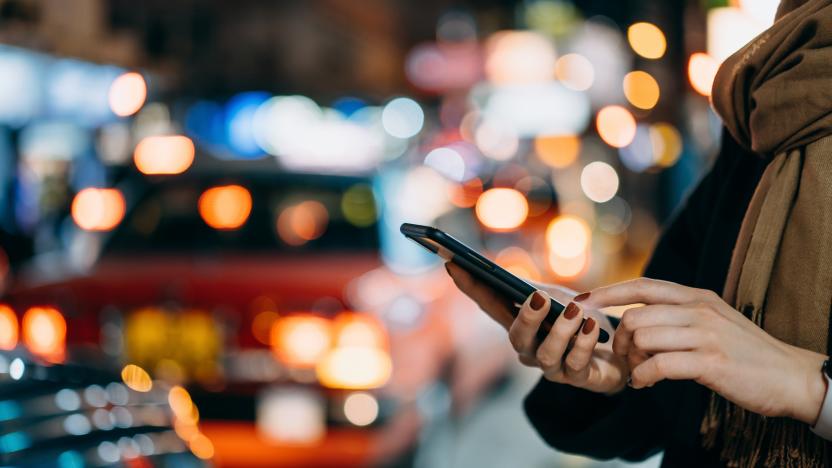 Close up of young woman using mobile app device on smartphone to arrange taxi ride in downtown city street, with illuminated busy city traffic scene during rush hour with traffic congestion in the evening