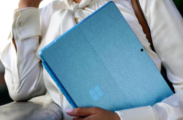 Lifestyle image of the Microsoft Surface Pro 9. A person holds a blue (patterned) version of the hybrid device (back-facing).