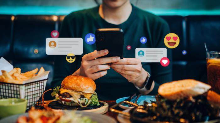 Cropped shot of young Asian woman using smartphone on social media app during meal in restaurant. Viewing posts, giving like, love, comment, making friends on pages in the city. People engaging in networking with technology. Social media addiction concept