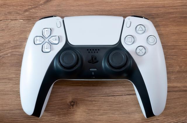 Closeup photo of a PS5 DualSense controller (white) sitting on a brown wooden surface.