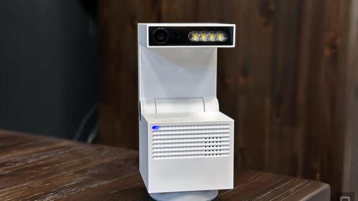 Image of the Psync Genie S AI-enabled home security camera in its default upright position on a wooden table with a wooden cabinet in the background