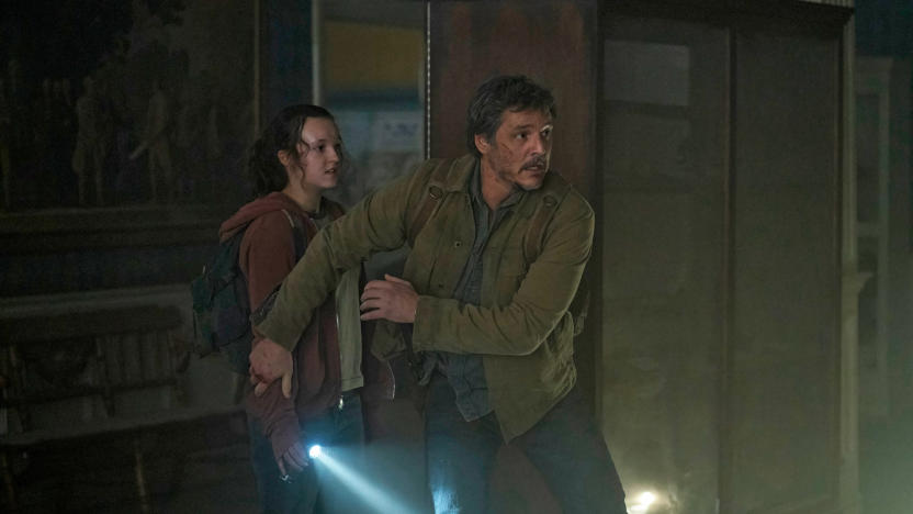 A promo image with Pedro Pascal and Bella Ramsey in HBO's The Last of Us. The two huddle in a dark corner of the room with a single flashlight, worried about some danger in the vincinity.