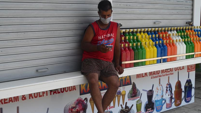 A man checks his mobile phone sitting outside a closed shop during restrictions imposed by state government amidst rising Covid-19 coronavirus cases, in Mumbai on April 15, 2021. (Photo by INDRANIL MUKHERJEE / AFP) (Photo by INDRANIL MUKHERJEE/AFP via Getty Images)