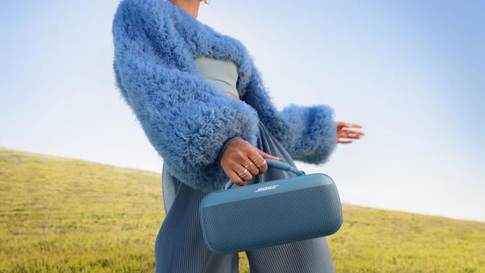 A person in a meadow holding a blue Bose SoundLink Max speaker. 