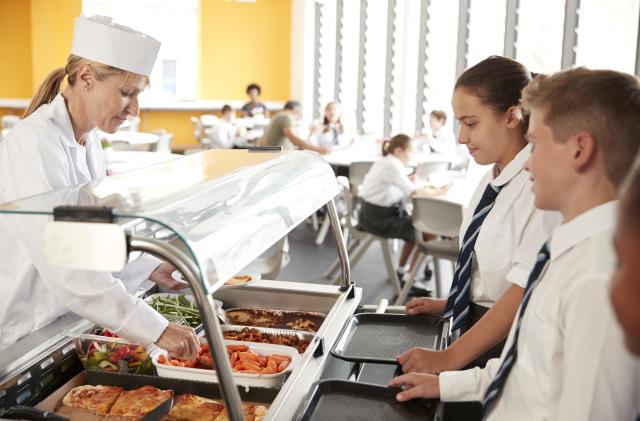 High School Students Wearing Uniform Being Served Food In Canteen