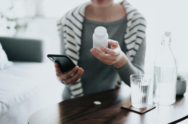 Close up of young Asian woman holding a pill bottle, consulting to her family doctor online in a virtual appointment over the smartphone at home