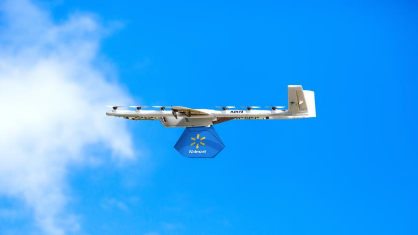 A white delivery drone carrying a blue Walmart bag soaring across a blue sky. Side view of the drone as it flies right to left across the frame.