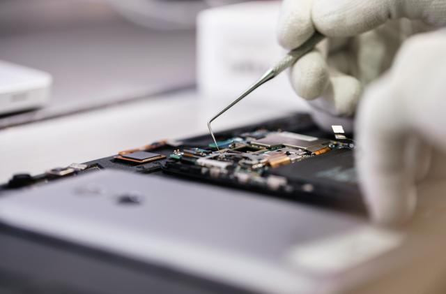 Work with a microscope. Microelectronics device. Close-up hands of a service worker repairing modern smartphone.