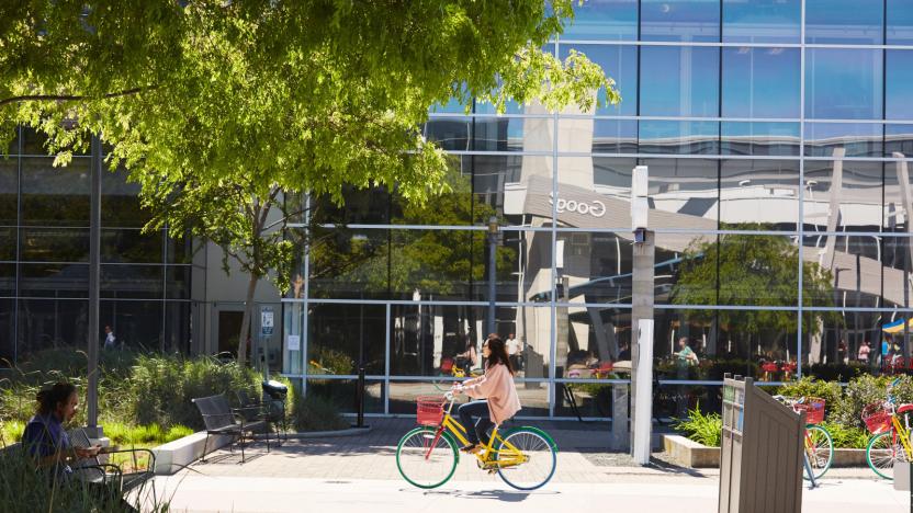 A  person riding a bike in front of a building with a mirror facade.