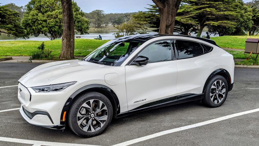 The Ford Mach-E EV in white parked in a lot by a park.