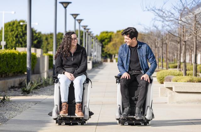 Two people sitting on high-tech chairs in the park.