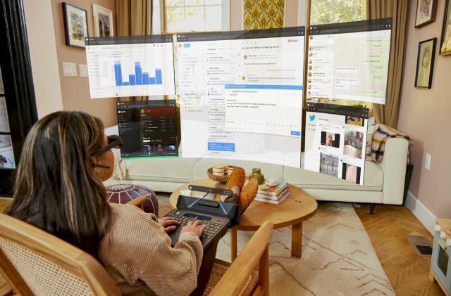 A woman uses Spacetop in her living room, which displays virtual computer desktop windows on a curved space in front of here via Augmented Reality (AR) glasses.