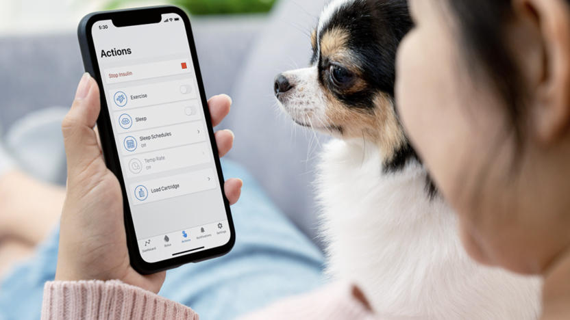 A person holding a phone showing the interface of a diabetes care app, with a dog next to them.