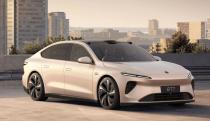 Marketing image of the Nio ET7 EV. The goldish-beige car sits on a lot overlooking a city skyline during daytime.